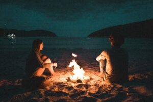 Man and woman sit by a fire, in the sand, at the seashore. For a blog post by Sabrina Walters about substance abuse recovery.